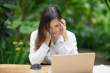 Young woman experiencing stress or frustration while working on a laptop in a serene outdoor environment surrounded by lush greenery and plants