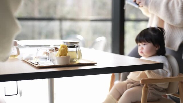 Soft light fills a cozy cafe. Child sits quietly, eyes wide. An adult reaches across the table. The child waits patiently. Warm tones suggest comfort. Perfect for family or parenting content