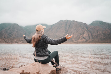 Woman in puffer jacket enjoying a cold mountain lake view with misty peaks © Jezabel