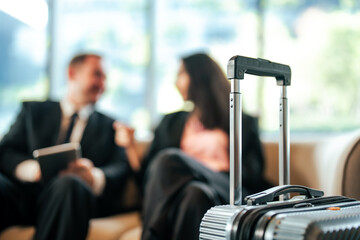 Close-up of a silver suitcase handle with business professionals blurred in the background. This...
