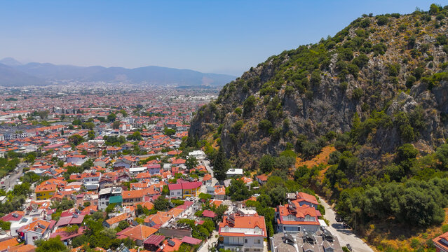 Fethiye, Turkey. Telmessos Lycian rock tombs overlooking modern Turkish city and residential houses, aerial drone view on sunny summer day.. Aerial View