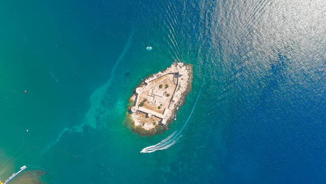 Kizkalesi, Mersin, Turkey. Dynamic parasail flight over Maiden Castle island fortress, surrounded by waves and rocks, towed by speedboat.. Aerial View