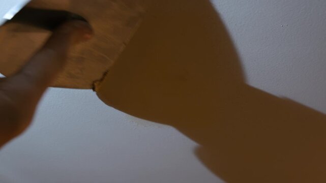 Close up view of Worker applying wall putty with a spatula to repair surface imperfections. Interior renovation process showing smoothing and preparation of wall before painting in a home improvement