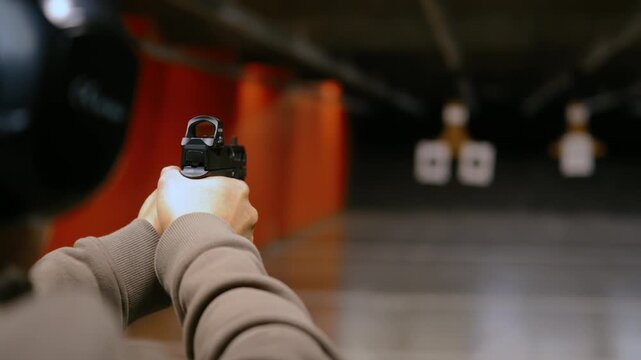 POV shot of person actively shooting handgun at paper targets inside an indoor shooting range. Controlled firearm use, marksmanship training, safe target practice.