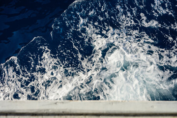 Obraz premium Top view of churning sea water and white wake from a sailing vessel. Abstract natural texture of blue ocean with sea foam. Concept of summer vacation, sailing adventure and marine transportation