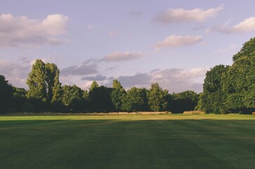 Naklejka premium A serene wide-angle view of a lush green park at sunset evoking peace and tranquility for travel and wellness website backgrounds.