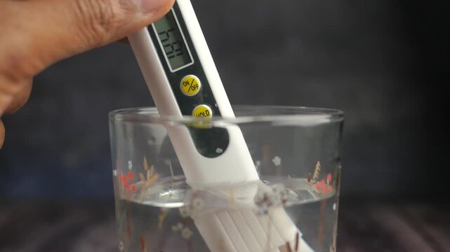 A hand holding a digital tds meter and testing water quality in a glass, close-up motion shot.