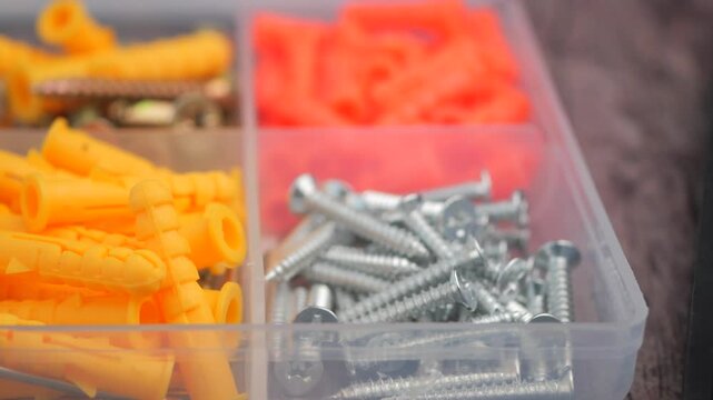 Close up of assorted hardware screws and wall anchors in a plastic organizer box.
