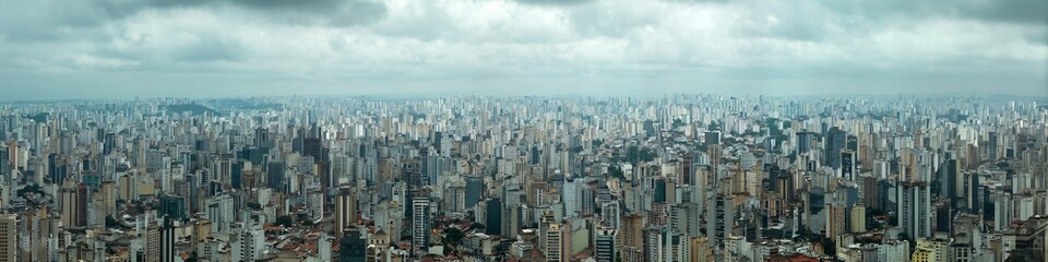 Fototapeta premium Cityscape Panorama under Cloudy Sky: Capturing the vastness and density of an urban landscape, rows of skyscrapers and buildings stretch towards the horizon under a dramatic, cloudy sky.