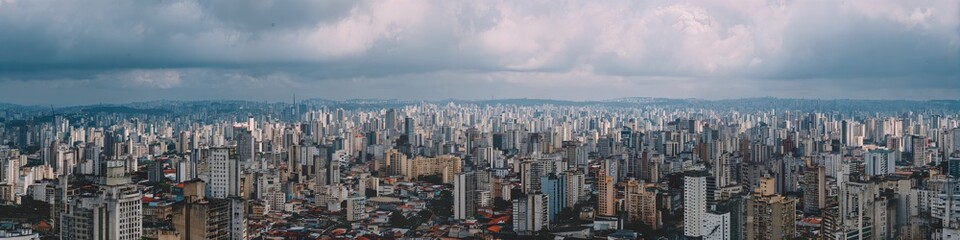 Obraz premium Cityscape Under Cloudy Sky: A sprawling cityscape stretches out beneath a dramatic, cloud-filled sky, creating a sense of urban density and scale.