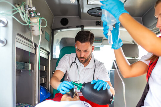 Paramedic using resuscitator bag for emergency ventilation on patient inside ambulance. Medical team providing life-saving treatment during transport. Healthcare and medicine concept, critical care.