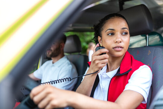 Female paramedic using walkie-talkie radio in ambulance. Professional emergency medical responder communicating with hospital dispatch. Healthcare and medicine concept, first responder coordination.