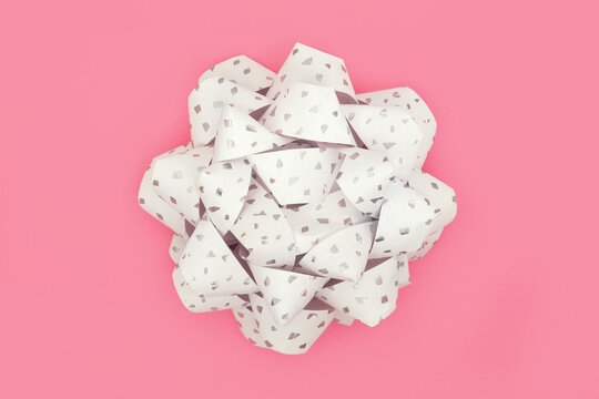 White silver ribbon gift bow for present, greeting card, gift tag, label. Decorative art abstract design on pink background, copy space.