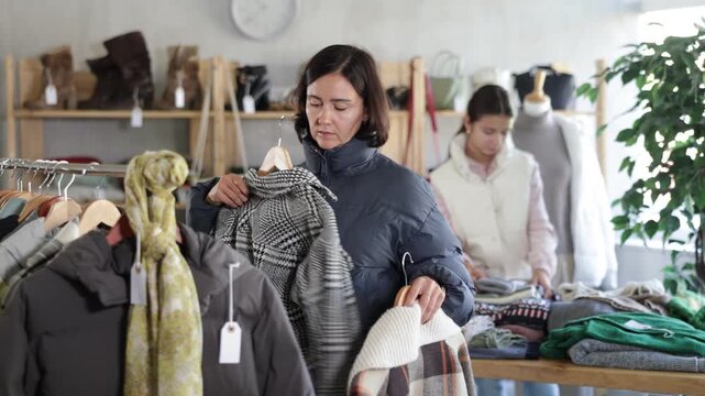 Adult woman buyer choosing warm coat or down jacket in clothing store