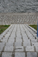 Fototapeta premium Stone steps leading to cobblestone riverside walkway along calm river water