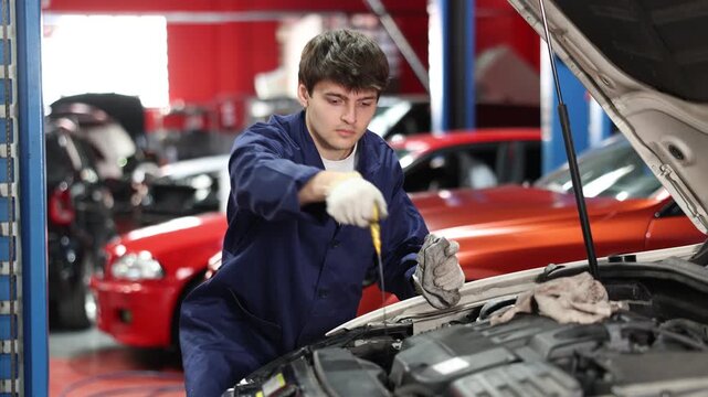 Qualified mechanic in a car service checks the amount of oil in the car with a dipstick. Car service employee inspects the car and changes the engine oil. High quality 4k footage