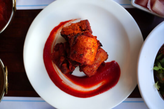 Authentic Indian Chicken Tikka served with spicy red sauce on a white plate.
