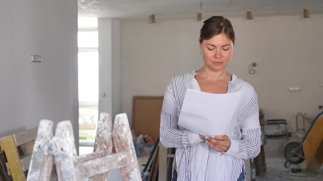 Young woman construction manager checking project documentation while working in apartment.
