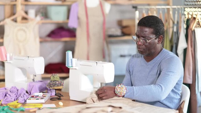 Male clothing designer stitching fabric on sewing machine in studio 