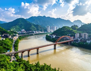 Obraz premium A vibrant aerial view showcases a modern arch bridge gracefully spanning a wide river, nestled amidst lush green hills and a developing cityscape under a bright, partly cloudy sky.