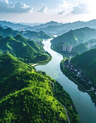 Obraz premium An aerial view showcases a winding river gracefully carving its path through lush, green mountains, with a distant cityscape subtly blending into the horizon under a bright, partly cloudy sky.