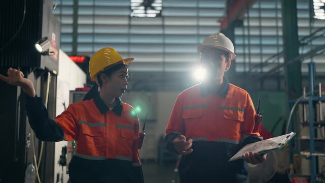 Collaborative Precision in Industrial Setting: Two professionals, clad in protective gear, engage in a focused discussion amidst the machinery of an industrial plant.