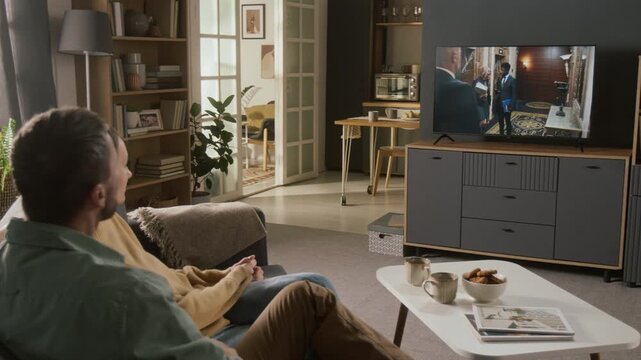 Medium arc shot of smiling Caucasian couple relaxing on couch in living room, watching legal drama on TV of lawyers having business negotiations, while chatting and discussing plot