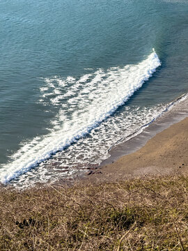 Challaborough Devon UK. 21.03.2026. A serene view of a breaking wave on a tranquil beach, with dry vegetation in the foreground, evoking a sense of natural coastal beauty