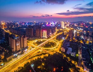 Obraz premium An aerial view captures a sprawling cityscape at twilight, showcasing a complex highway interchange illuminated by vibrant lights against a colorful sunset sky.