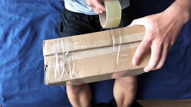 Man wraps a cardboard box with packing tape, top view