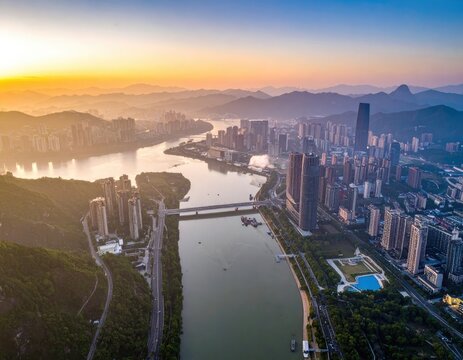 An aerial view captures a sprawling cityscape nestled along a winding river, bathed in the warm hues of a vibrant sunset, showcasing a blend of urban development and natural beauty.