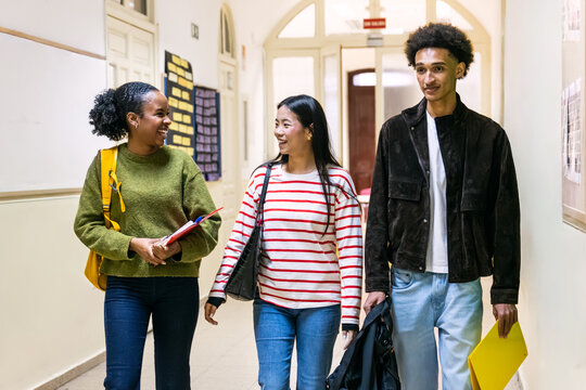 Diverse group of college students walking and smiling in a university hallway, carrying books and sharing a moment between classes