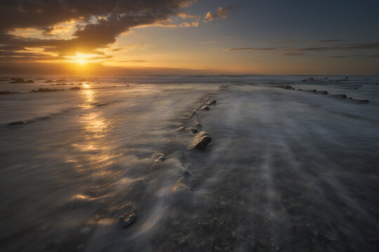 Dramatic flysch rock formations on the shore of Barrika beach during a cloudy sunset in Bizkaia