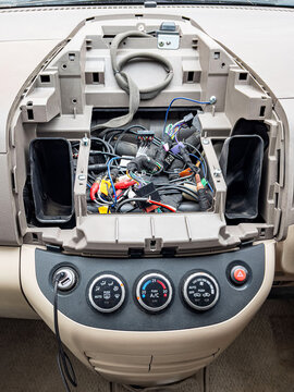 Exposed car dashboard with tangled wiring and removed stereo unit, closeup of beige interior, scattered connectors and cables, DIY installation scene