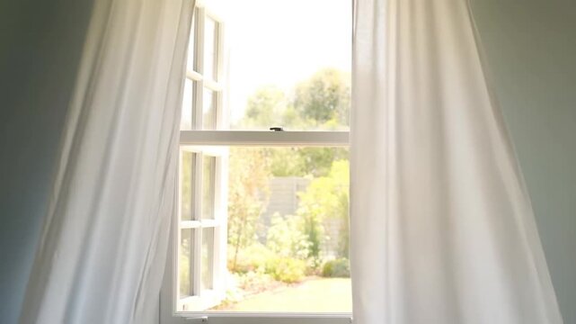 Window, two long white linen curtains softly billowing and swaying from the airflow of an open window, alternately revealing and concealing a view of a sunny garden, concept of gentle movement and fil