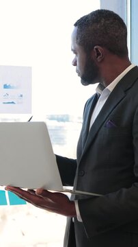 An African American businessman reviews financial charts and graphs while holding a laptop, indicating a focus on data-driven decision-making