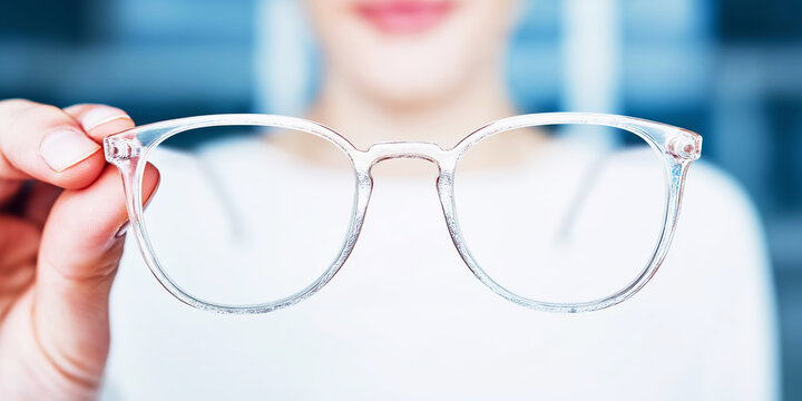 Woman presenting transparent vintage style eyewear frames holding them near soft sunlit window