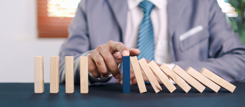 Businessman hand stopping falling domino blocks to prevent chain reaction, symbolizing risk control, leadership, and strategic decision making