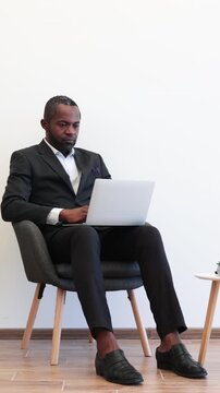 An African American man in a suit sits thoughtfully with a laptop on his lap, contemplating his next move