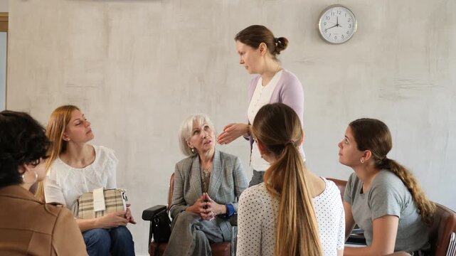 Female colleagues sit in semicircle during meeting and discuss plans to resolve situation.active participant of meeting stands and offers solution to issue