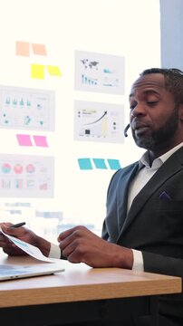 A headset-wearing consultant reviews charts and sticky notes during a virtual briefing in a bright office