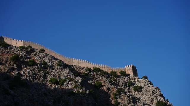 Ancient medieval Alanya Castle wall on rocky mountain ridge against deep blue sky. Historical landmark in Turkey, fortification. Defense, heritage, fortress architecture and travel concept, tourism