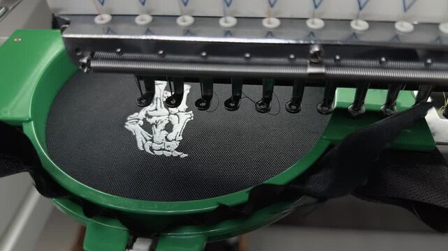 High Speed Industrial Embroidery Machine Head Stitching White Thread Design on Black Fabric in Professional Textile Workshop Handheld Slow Motion Close Up Authentic Production Manufacturing Video