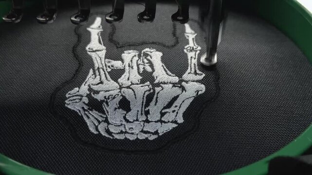 Macro Close Up Industrial Embroidery Machine Finishing White Skeleton Hand Rock Sign Design on Black Fabric Handheld Slow Motion Authentic Production