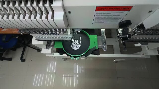 Wide Angle Establishing Shot of Automated Industrial Multi-Head Embroidery Machine Stitching White Skeleton Hand Rock Sign Logo on Black Fabric in Factory Handheld Slow Motion Authentic Scene