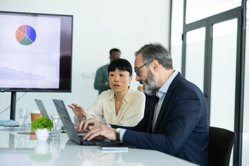 Fototapeta premium Diverse business people discussing data analysis, working on strategy in a modern conference room, promoting teamwork and communication