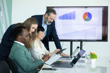 Naklejka premium Multicultural business team working together in an office meeting, reviewing financial data and charts on a large screen