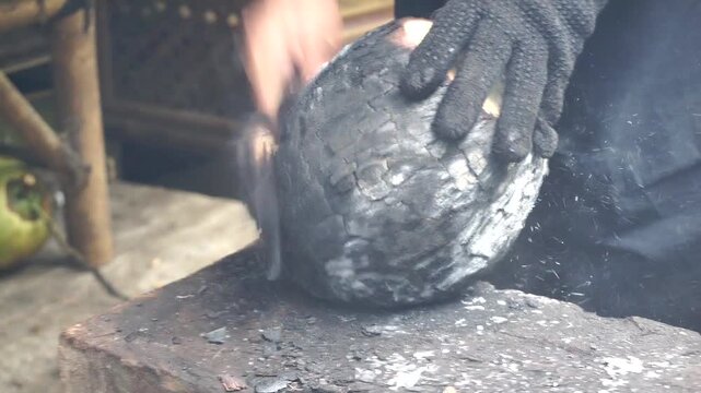 Manual activity of opening roasted coconut shell as part of preparing a natural healthy drink.