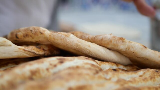 Freshly baked traditional flatbread stacked in rustic bakery with blurred artisan baker too.