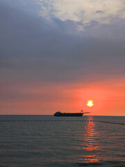 A warm sunset over a calm sea with the reflection of the sun and the dark silhouette of a ship on the horizon creates an atmosphere of privacy.  © Oksana